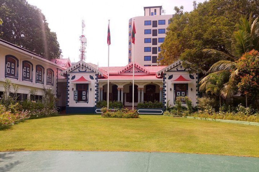 Un edificio con techo rojo y paredes blancas, rodeado de un césped cuidado y palmeras. 3