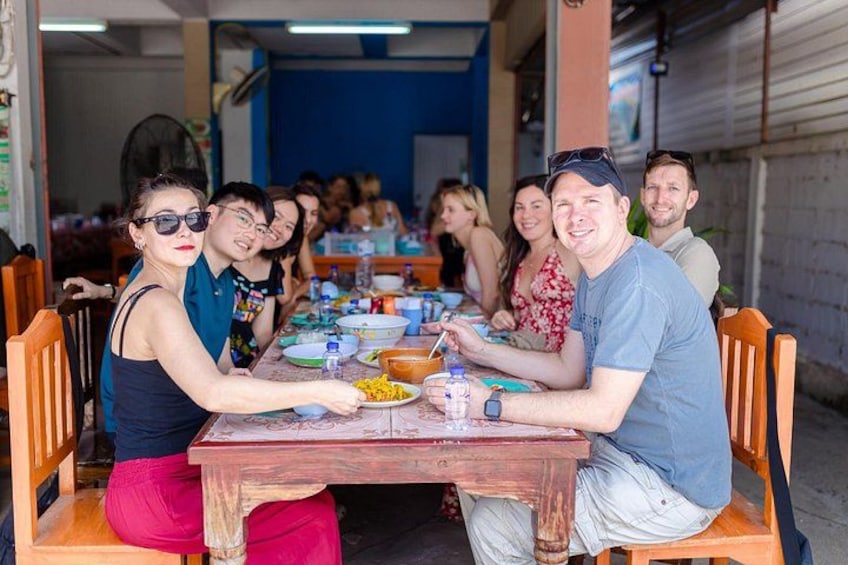 A group of people sitting at a wooden table outdoors, engaged in a meal. 2