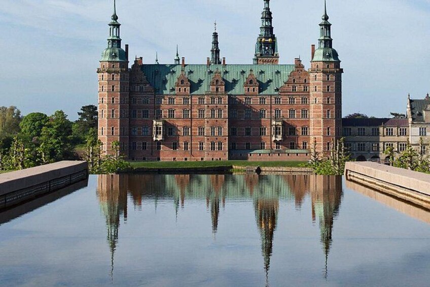 Un gran edificio histórico con múltiples agujas, su reflejo en un cuerpo de agua tranquilo, y un puente en primer plano. 2