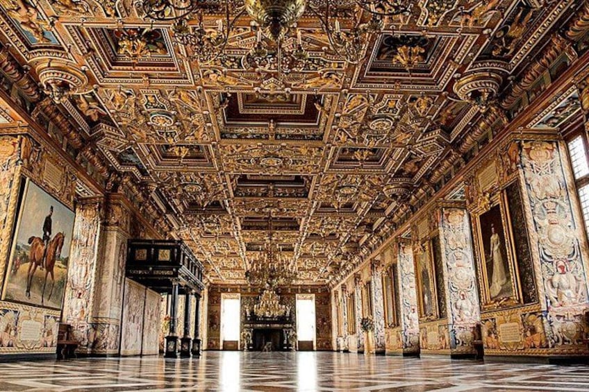 An ornate hall with intricate ceiling artwork, marble columns, and a checkered floor. 2