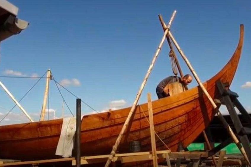 A wooden boat with a person working on it, a ladder, and a clear sky. 4