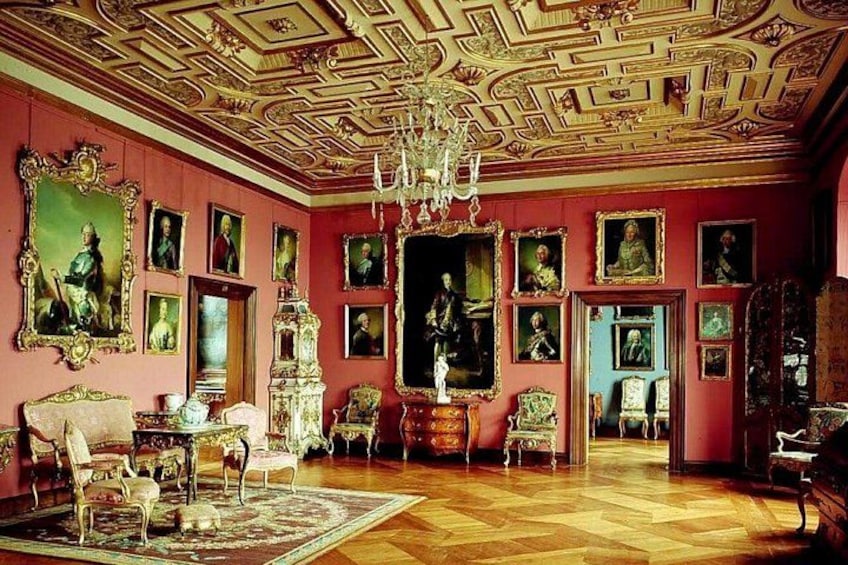 A richly decorated room with ornate furniture, a large chandelier, and numerous framed portraits on the walls. 3
