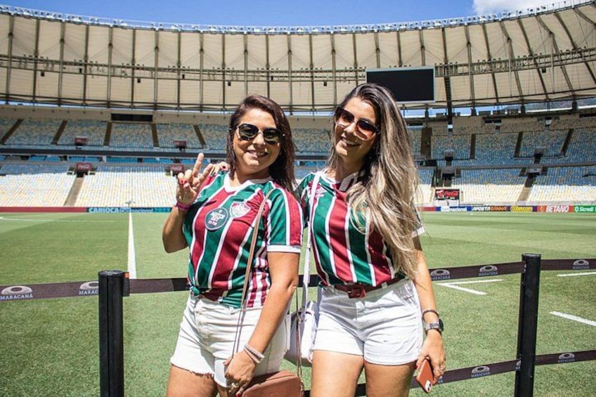 Two people in sports uniforms standing in a stadium with empty seats and a large screen. 2