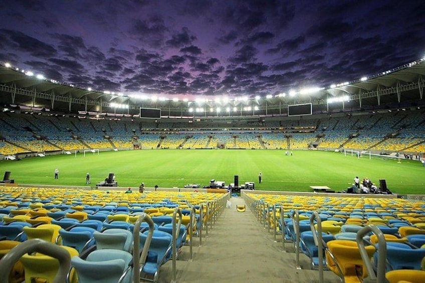 A large stadium with blue and yellow seats, a green field, and a dark sky. 3