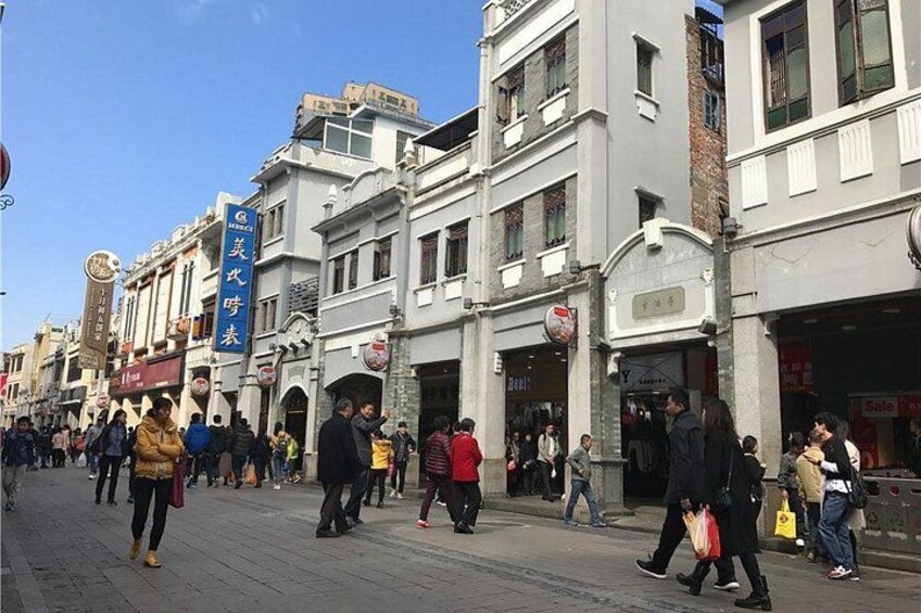 Eine belebte Stadtstraße mit Fußgängern, Geschäften und Beschilderung. 2