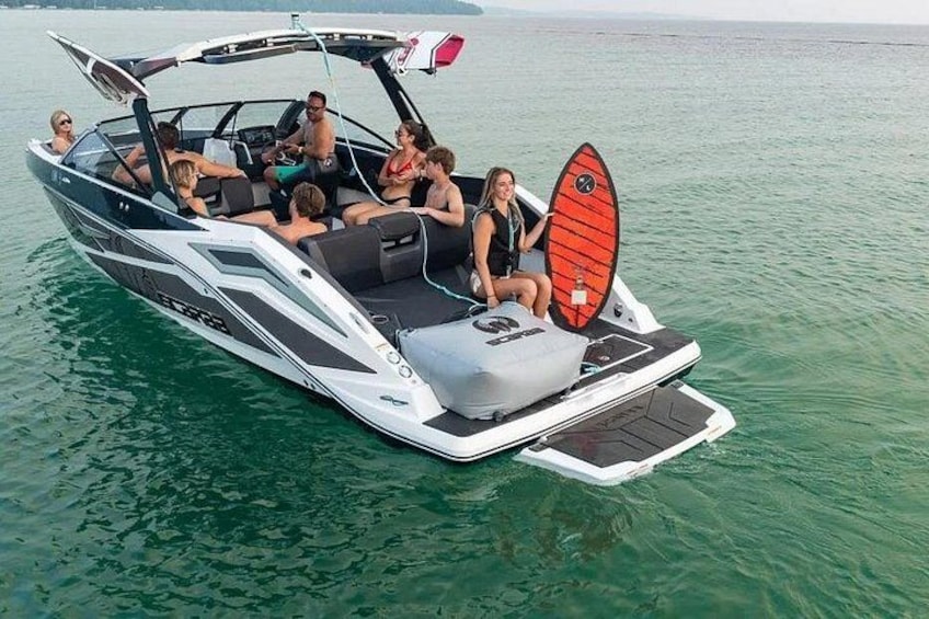 Een speedboot met een wakeboard achterop, mensen aan boord en rustig water. 2