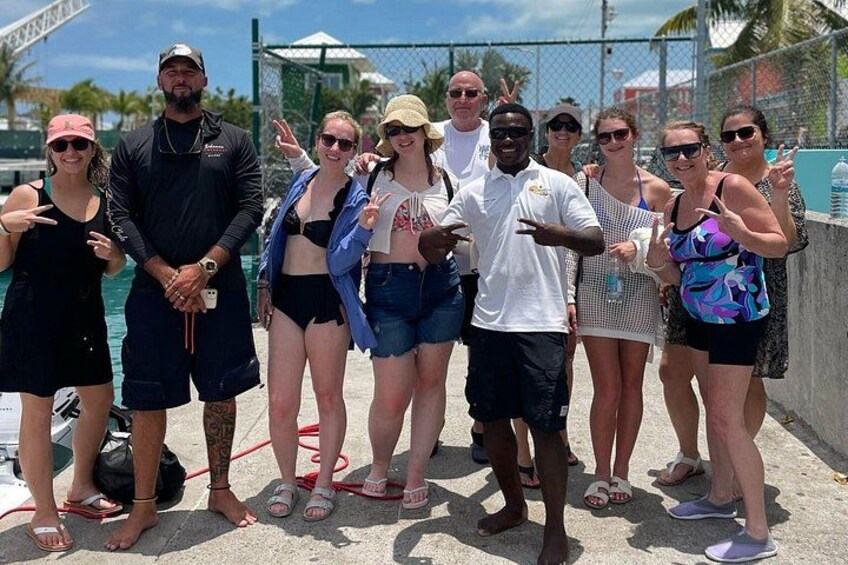 A group of people posing by a poolside with a fence and palm trees in the background. 5