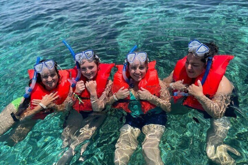 Four people snorkeling in clear water, wearing red life vests and blue snorkels. 5