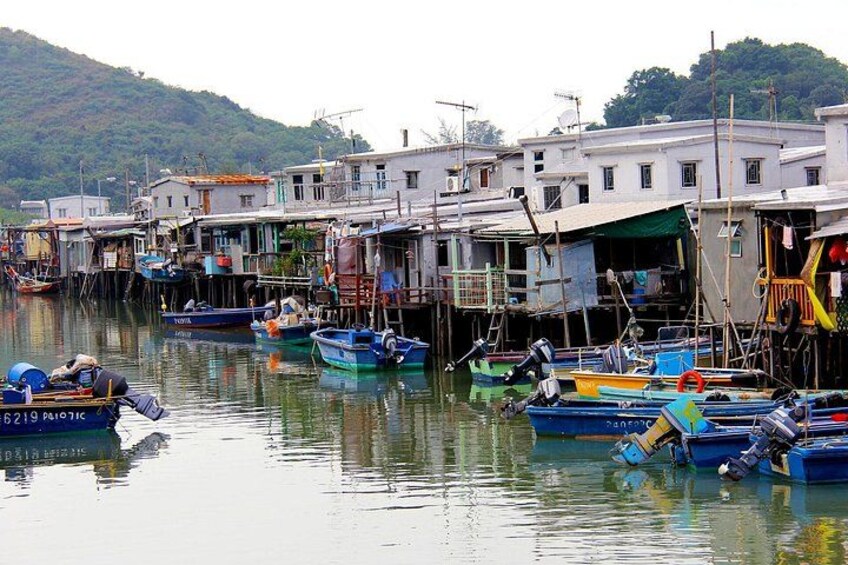 A waterfront with boats docked, buildings, and a hilly landscape in the background. 2