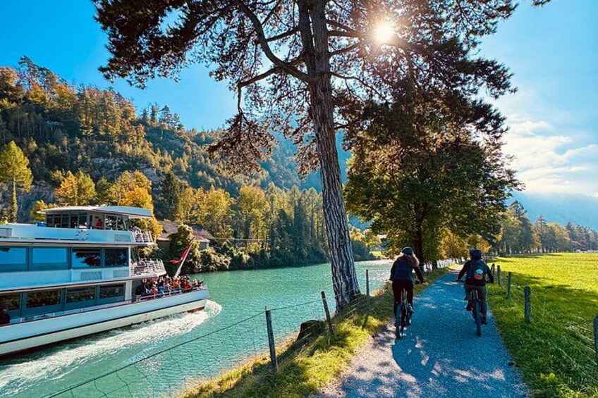 A river with a boat, a path with cyclists, and a forested hillside. 5