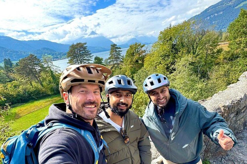 Three people wearing helmets and backpacks, standing on a rocky path with a mountainous landscape in the background. 3