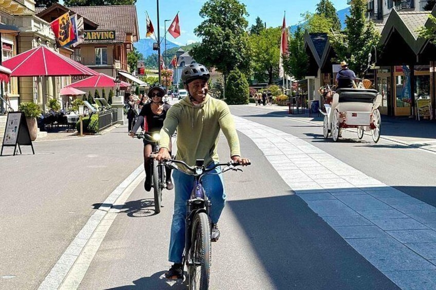 Une personne à vélo sur une piste cyclable, avec des bâtiments et des drapeaux en arrière-plan. 2