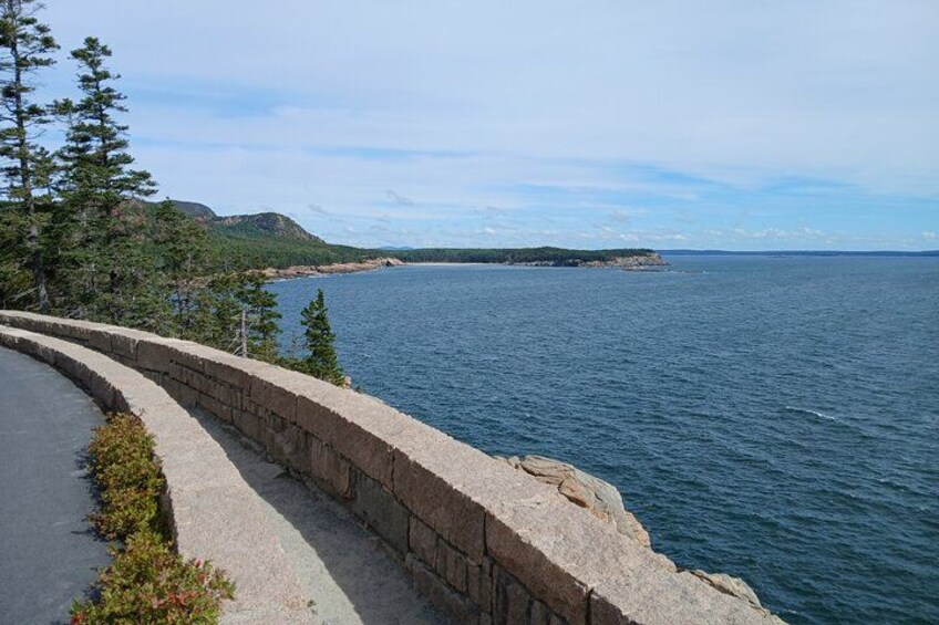 En kustväg med en stenmur, träd och utsikt över havet och det avlägsna landskapet. 5