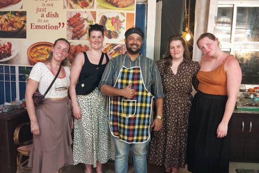 A group of people standing in a kitchen with a poster on the wall. 2