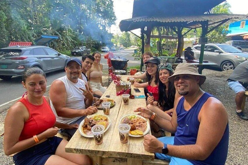 A group of people dining outdoors at a wooden table with food and drinks. 2