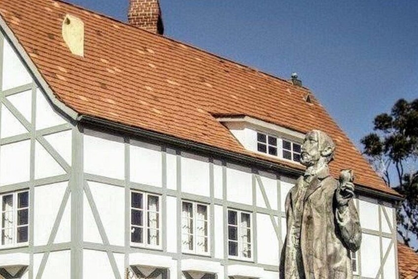Ein Gebäude im Tudor-Stil mit weißer Fassade und Fachwerkerbauweise, einem roten Ziegeldach und einer Statue eines Mannes, der ein Buch hält. 2