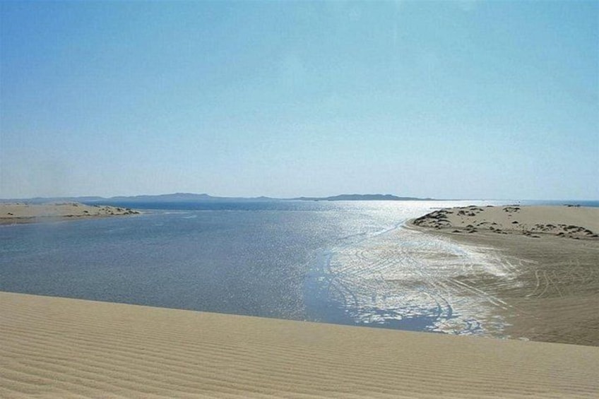 Eine Wüstenlandschaft mit Sanddünen und einem Gewässer, das den Himmel spiegelt. 3