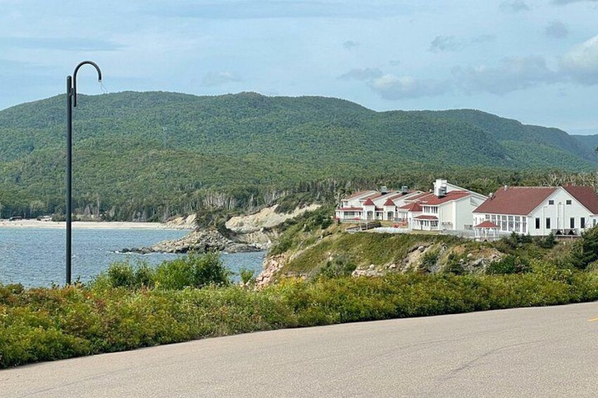 A coastal road with a white building complex, a curved street lamp, and a backdrop of green hills. 5