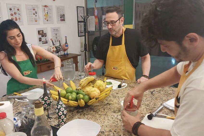 Des personnes préparent des aliments dans une cuisine, sur le plan de travail duquel on peut voir une variété de fruits et de légumes. 3