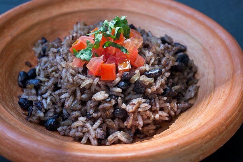 Un bol en bois rempli de riz noir, garni de tomates coupées en dés et d’herbes aromatiques. 5
