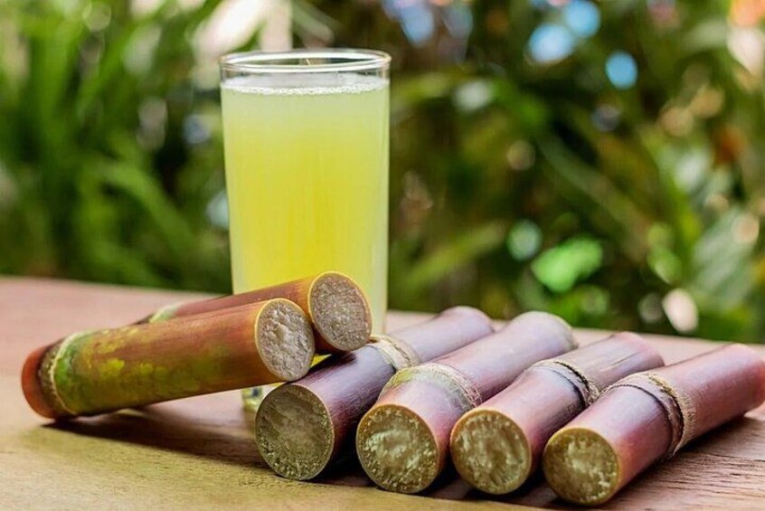 Un verre contenant un liquide jaune, peut-être du jus, et plusieurs morceaux d’un fruit ou d’un légume de couleur rouge-brun, coupés, sur une surface en bois, avec un feuillage vert en arrière-plan. 4