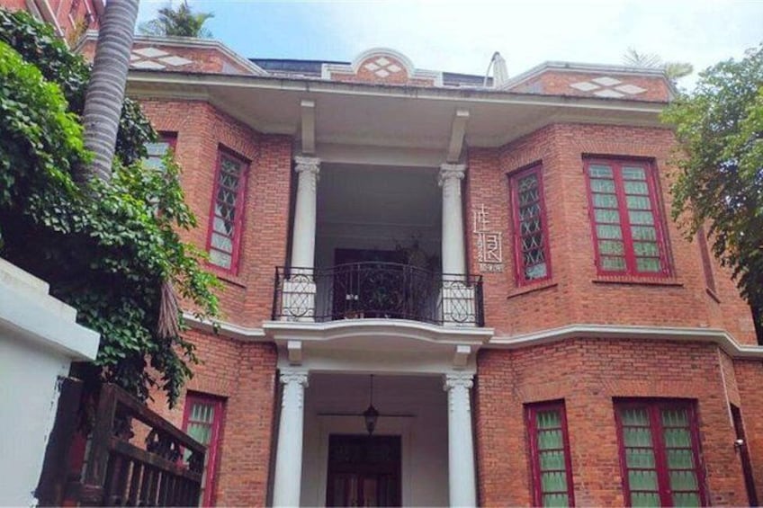 A red brick building with a balcony, white columns, and green window shutters. 3