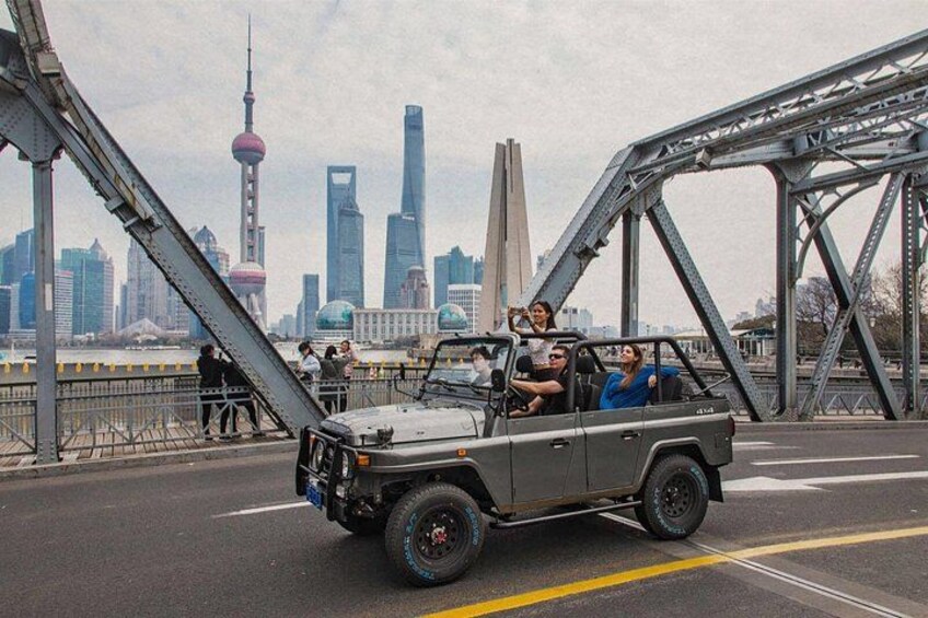 A vehicle with passengers on a bridge with a city skyline in the background. 1