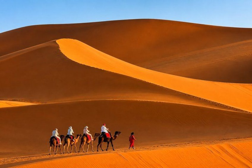 A desert landscape with sand dunes and people riding camels. 2