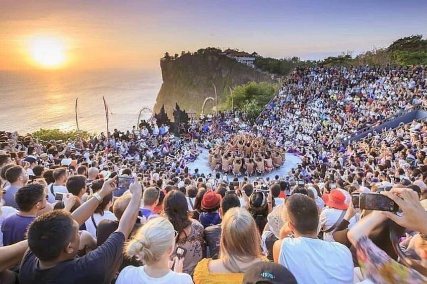 Eine große Menschenmenge hat sich für eine Veranstaltung am Küstenstreifen versammelt, im Hintergrund ist ein Sonnenuntergang zu sehen. 3