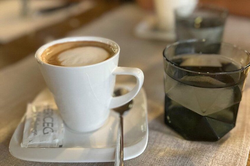 A white cup of coffee with a spoon on a saucer, a glass of water, and a packet of sugar on a table. 3