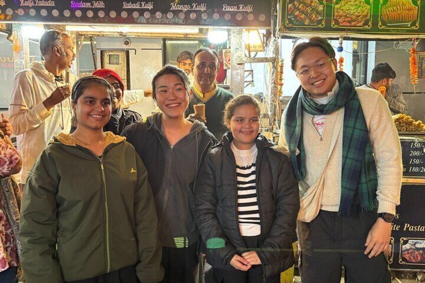 A group of people at a food stall with various food items displayed. 1