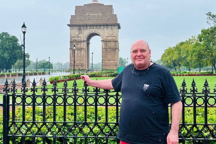 A man standing in front of the India Gate with a park and a river in the background. 3