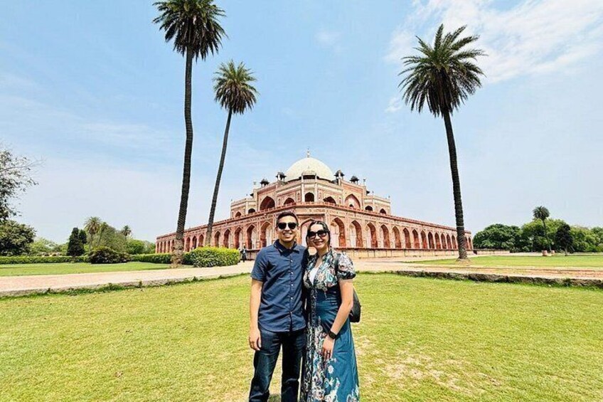 A couple standing in front of a large, historic building with a dome, surrounded by palm trees and a well-maintained lawn. 3