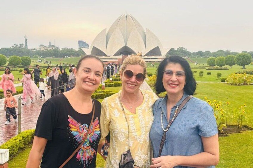 Three people standing in front of a large, modern building with a unique architectural design, surrounded by well-maintained gardens and a crowd of visitors. 2