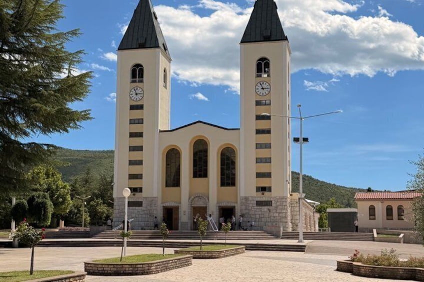 A church with two towers and a clock, surrounded by a landscaped garden and a mountainous backdrop. 2