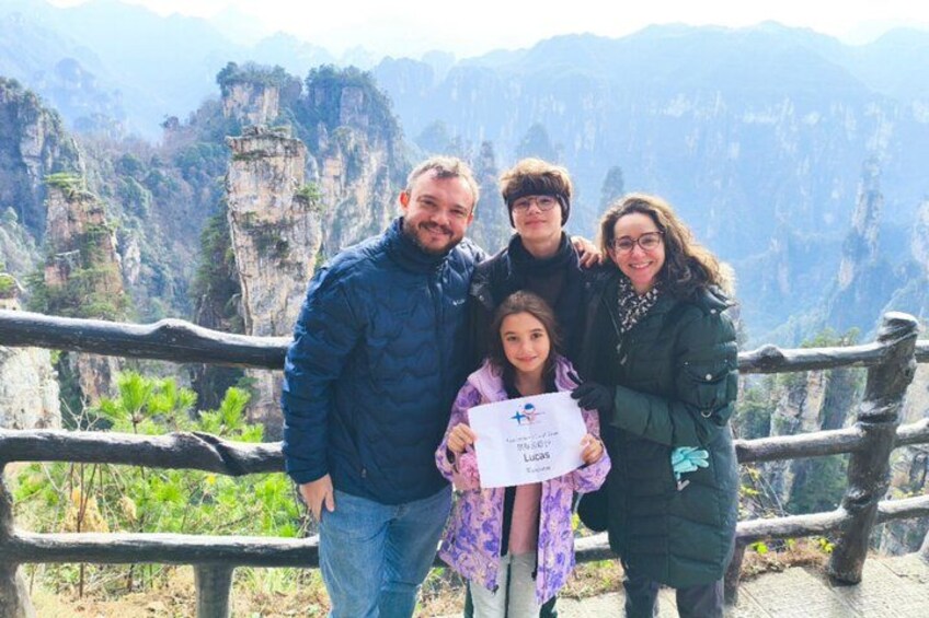 A family of five standing on a wooden platform with a scenic mountainous landscape in the background. 2