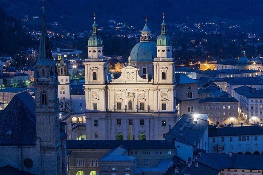A historic cathedral with two domes and a bell tower, surrounded by city buildings at night. 3