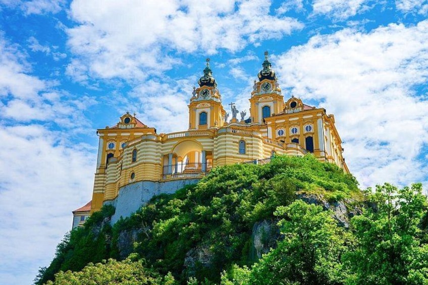 A yellow church with two towers, surrounded by greenery and a clear sky. 1