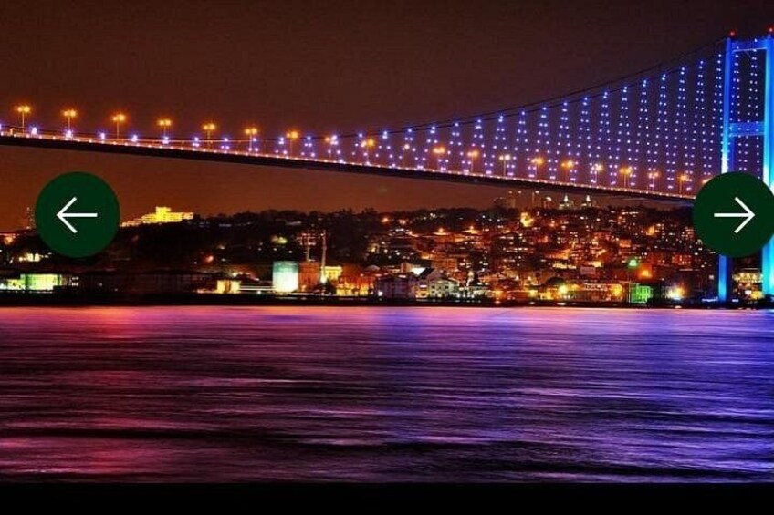 A bridge with lights, a body of water, and a cityscape in the background. 1