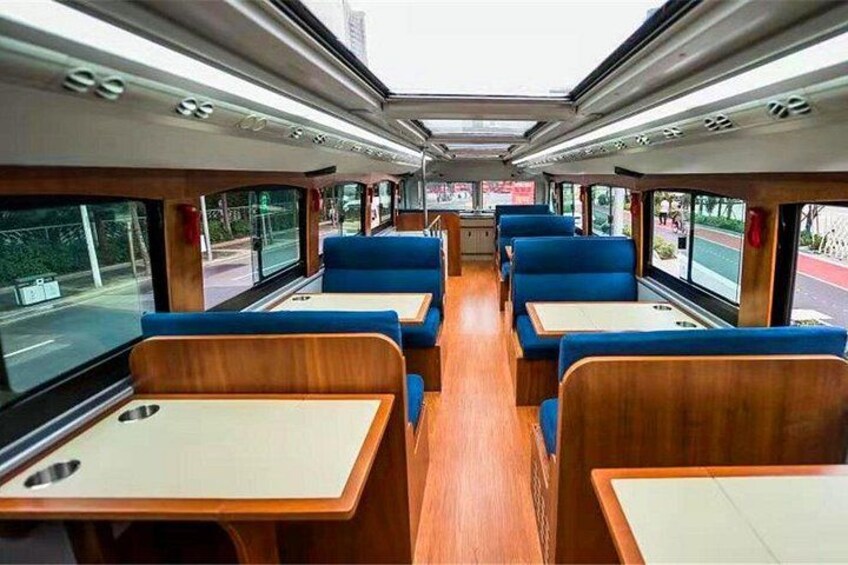 A train interior with blue upholstered seats, wooden tables, and large windows. 2