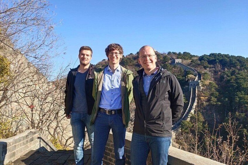 Three people standing on a stone wall with a mountainous landscape in the background. 5