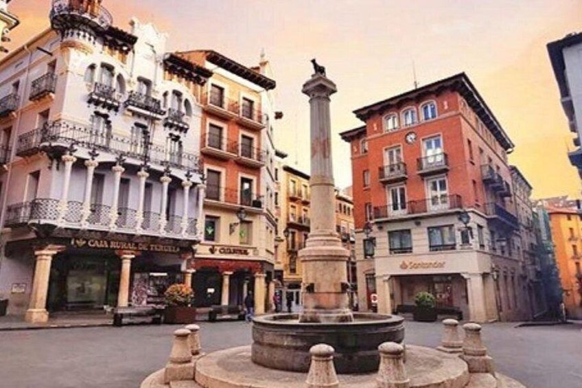 A plaza with a central fountain, surrounded by historic buildings with balconies and storefronts. 5
