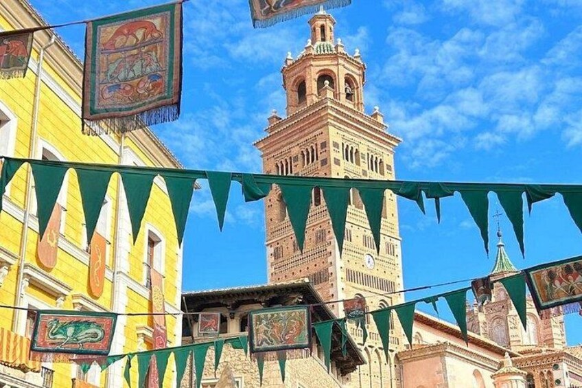 A historic tower with a clock, colorful buildings, and green triangular flags. 2