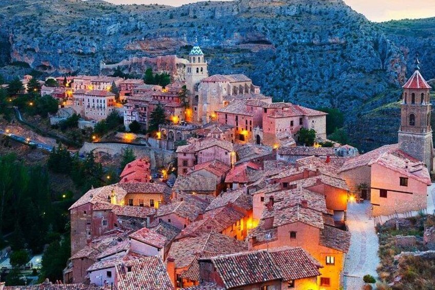 A historic town with terracotta-roofed buildings, a prominent church, and a bell tower. 1