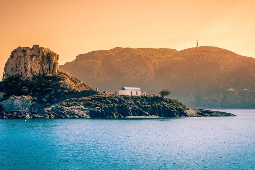 A coastal landscape with a white building on a rocky outcrop, a large cliff, and calm sea. 2