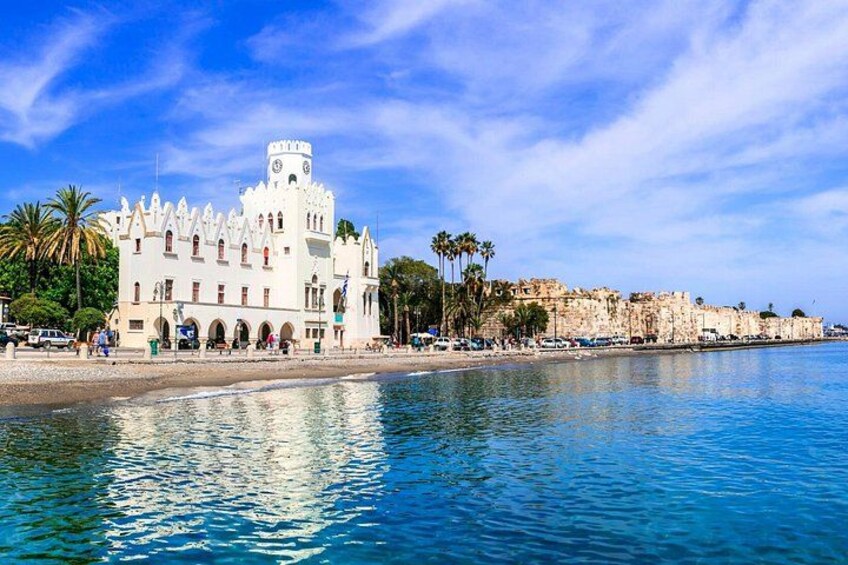 A coastal building with a clock tower, palm trees, and a clear blue sky. 1