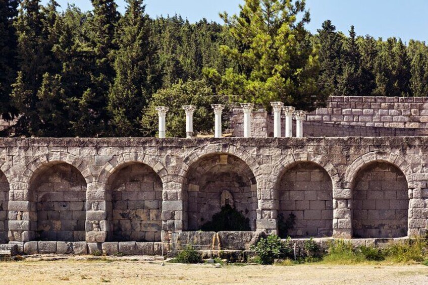A stone structure with arches and columns, surrounded by trees. 3