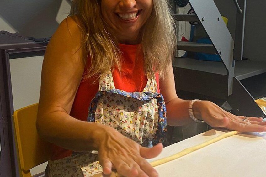 A person wearing a floral apron and a red top, seated at a table with a white surface, possibly engaged in a cooking or crafting activity. 5