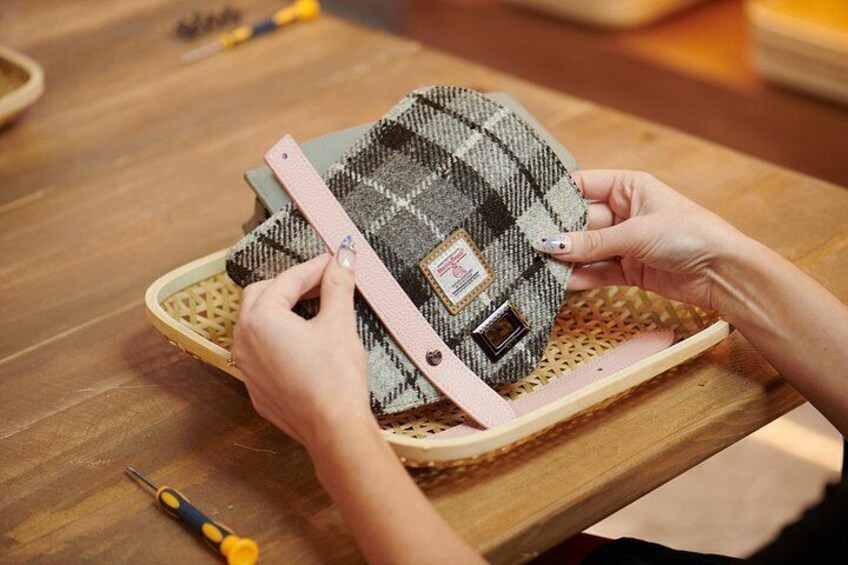 Manos armando una bolsa tejida con una hebilla metálica sobre una mesa de madera. 1