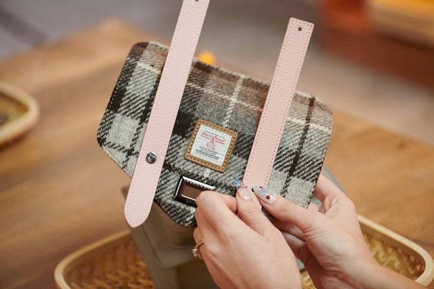 Hands attaching a plaid-patterned strap to a bag. 2